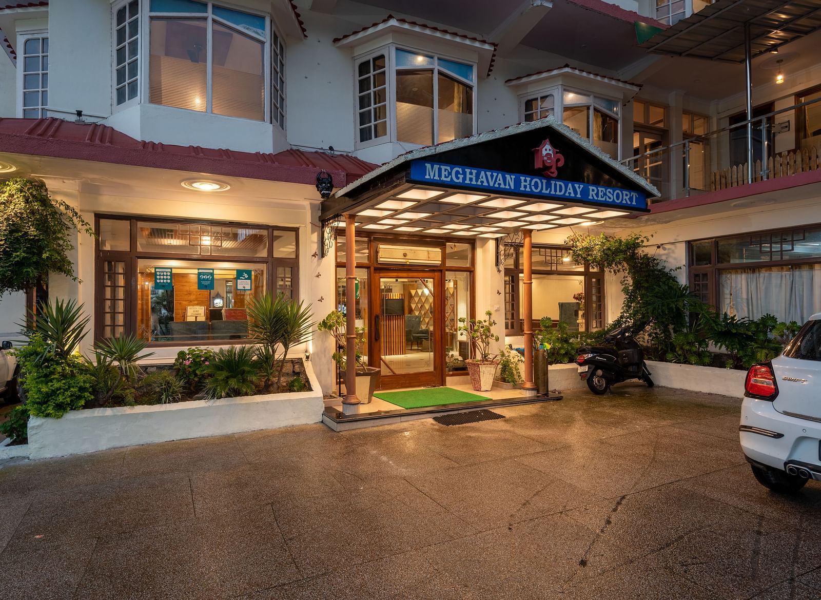 A photo of the entrance to DLS Meghavan Resort, showing the building's facade, entrance way, and some potted plants.